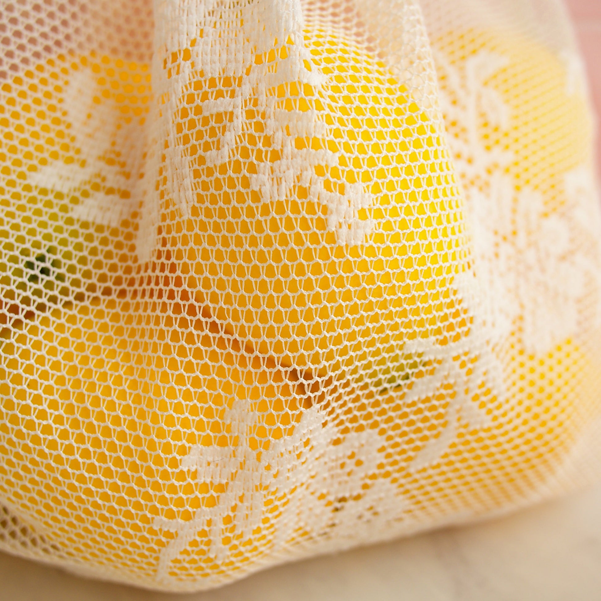 Close up image of lace on reusable lace produce bag, filled with lemons