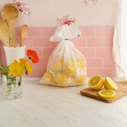 Reusable Produce bag made from lace, on a pink tiled backdrop, filled with lemons